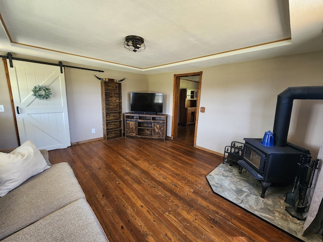 living room with wood-type flooring, a barn door, baseboards, and a wood stove
