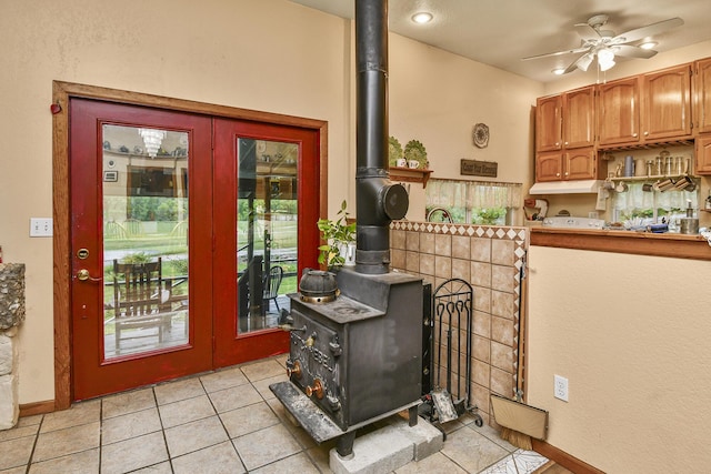 doorway to outside featuring a wood stove, ceiling fan, light tile patterned floors, and baseboards