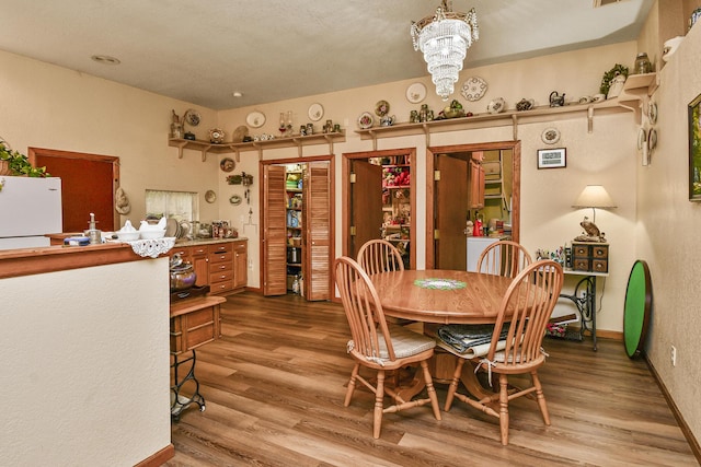 dining room with wood finished floors, a chandelier, baseboards, and a textured wall