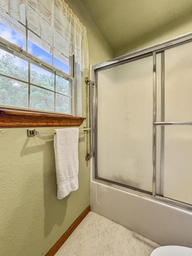 full bath with bath / shower combo with glass door, baseboards, toilet, and a textured wall