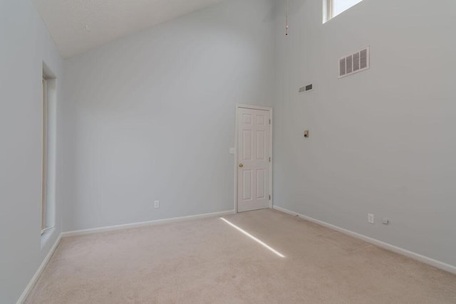 unfurnished room with light colored carpet, a towering ceiling, and baseboards