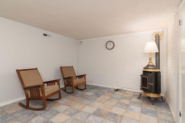 sitting room featuring stone finish floors, a wood stove, a textured ceiling, brick wall, and baseboards