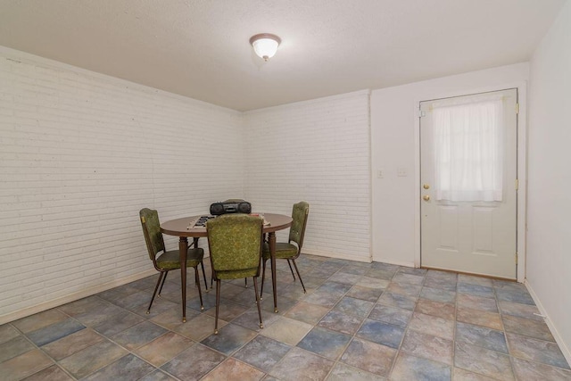 dining space featuring brick wall, baseboards, stone finish flooring, and a textured ceiling