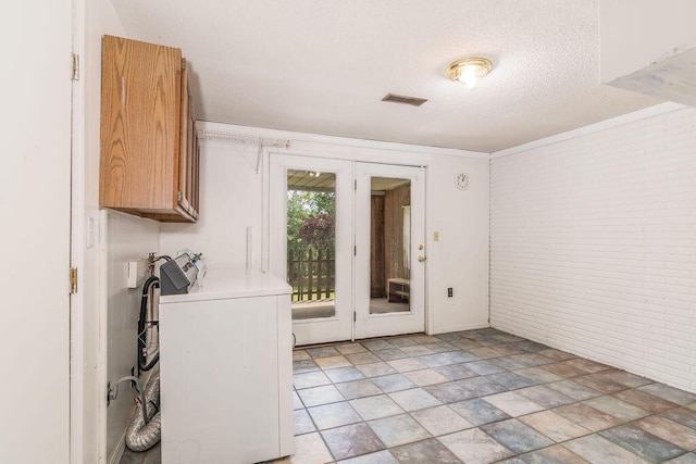 doorway with washer / clothes dryer, brick wall, a textured ceiling, and ornamental molding