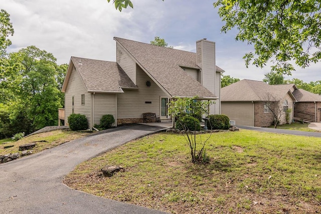 view of front facade featuring a chimney, roof with shingles, a front yard, and a garage