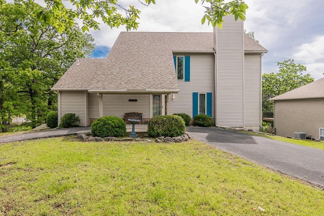 view of front of property featuring a front lawn, a chimney, central AC unit, and roof with shingles