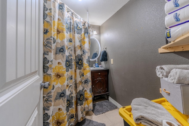 full bathroom featuring tile patterned floors, a shower with shower curtain, vanity, baseboards, and a textured wall