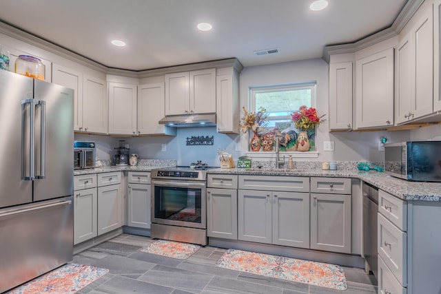 kitchen with appliances with stainless steel finishes, under cabinet range hood, recessed lighting, a sink, and light stone counters