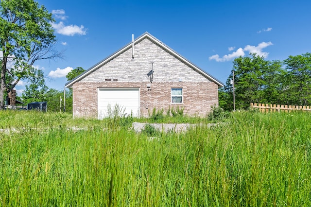 view of property exterior with brick siding, a detached garage, and fence