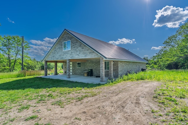 back of house featuring a patio, fence, metal roof, and stone siding