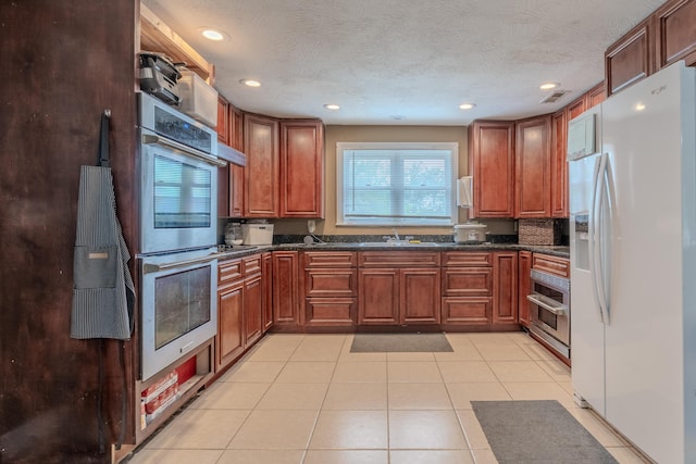 kitchen with white fridge with ice dispenser, double oven, dark countertops, a sink, and light tile patterned floors