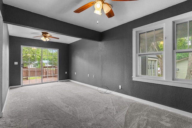 carpeted spare room with a ceiling fan, baseboards, and a textured wall