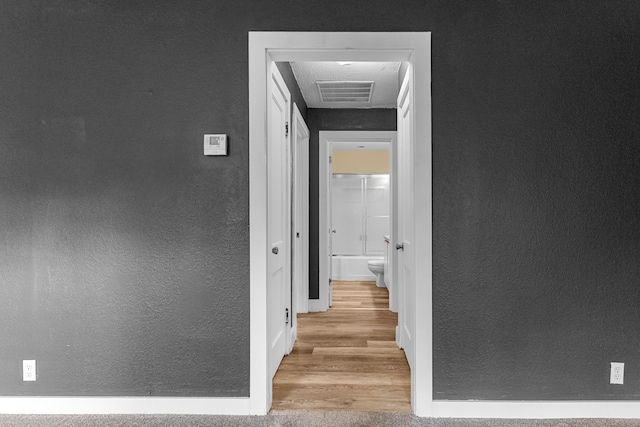 hall featuring a textured wall, baseboards, and wood finished floors