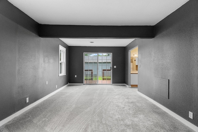 empty room featuring a textured wall, light colored carpet, and baseboards