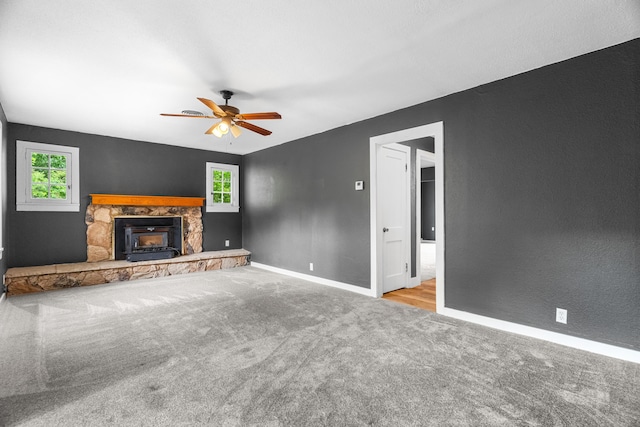 unfurnished living room with carpet flooring, a stone fireplace, baseboards, a ceiling fan, and a textured wall