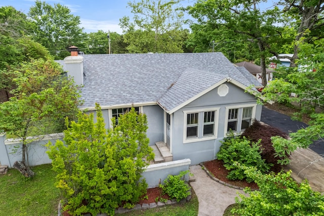 view of front of home featuring a shingled roof, stucco siding, and a chimney