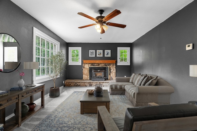living area with ceiling fan, a textured wall, a stone fireplace, and baseboards