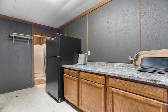 kitchen featuring freestanding refrigerator, light flooring, light stone countertops, and brown cabinets