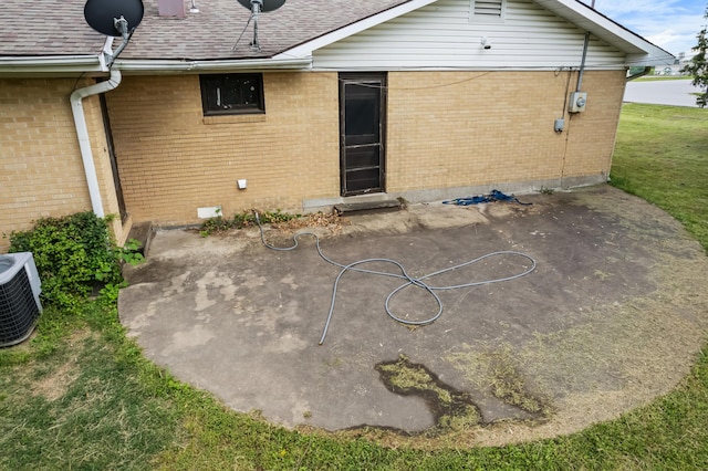 rear view of house with brick siding, a patio area, roof with shingles, and central AC