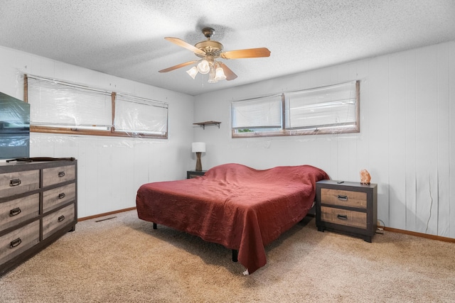 bedroom featuring light carpet, ceiling fan, a textured ceiling, and baseboards
