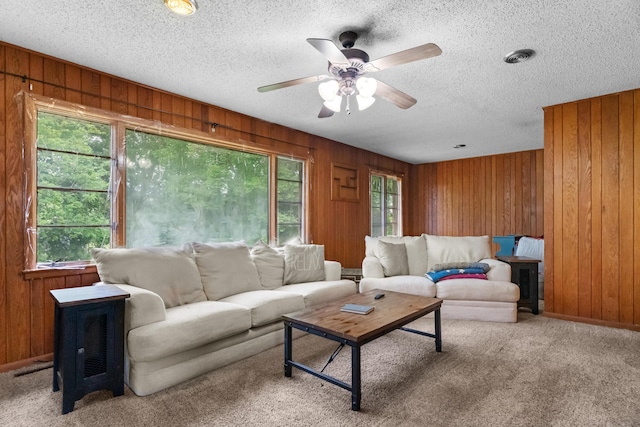 living area with wood walls, a ceiling fan, carpet floors, and a textured ceiling