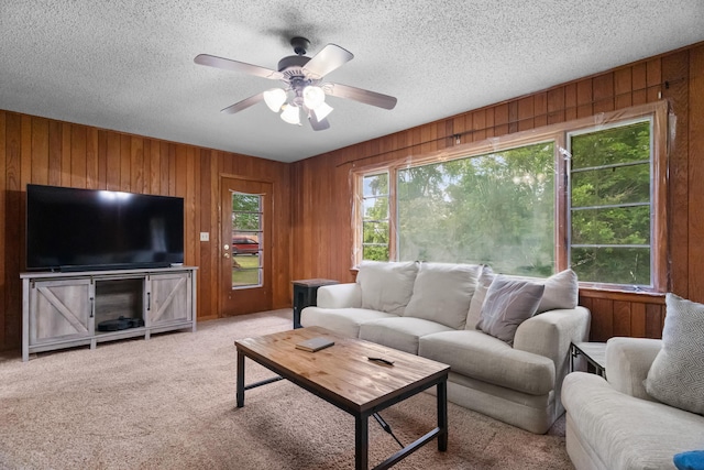 carpeted living area with wood walls, a ceiling fan, and a textured ceiling