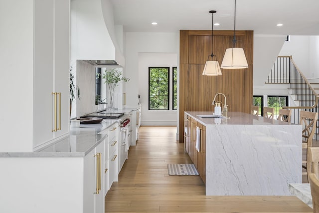 273 Secret Ln, Branson West, MO 65737 - kitchen featuring a sink, custom exhaust hood, light wood-style flooring, a kitchen island with sink, and white cabinets