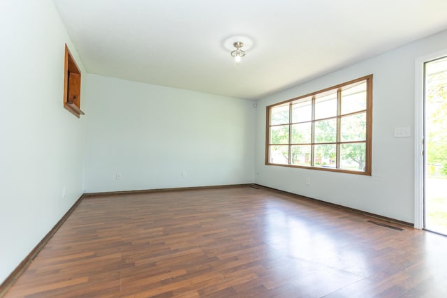 empty room featuring healthy amount of natural light, wood finished floors, and baseboards