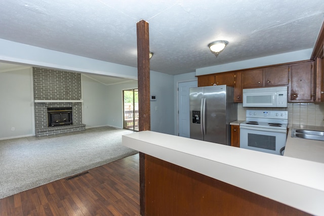 kitchen with white appliances, light countertops, dark wood-type flooring, a peninsula, and a brick fireplace