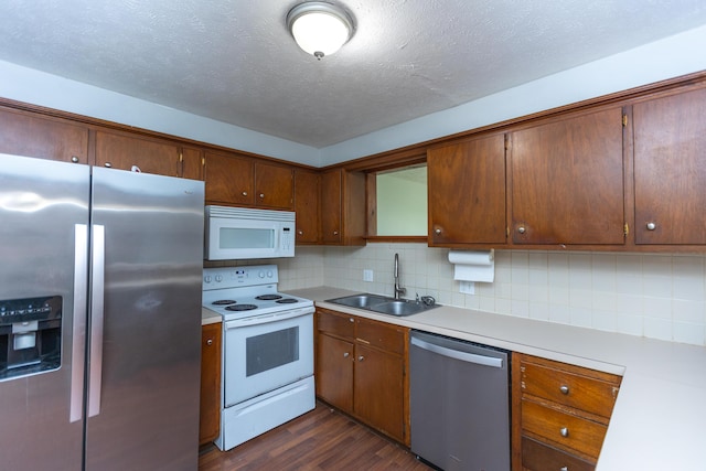 kitchen with appliances with stainless steel finishes, a sink, dark wood finished floors, light countertops, and a textured ceiling
