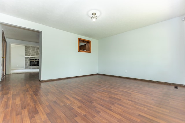 spare room featuring dark wood-style flooring, a fireplace, and baseboards
