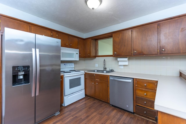 kitchen featuring appliances with stainless steel finishes, a sink, dark wood-type flooring, backsplash, and light countertops