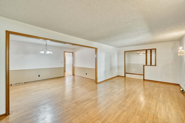 4852 S Charleston Ave, Springfield, MO 65804 - empty room featuring a chandelier, a textured ceiling, light wood-style flooring, and wainscoting
