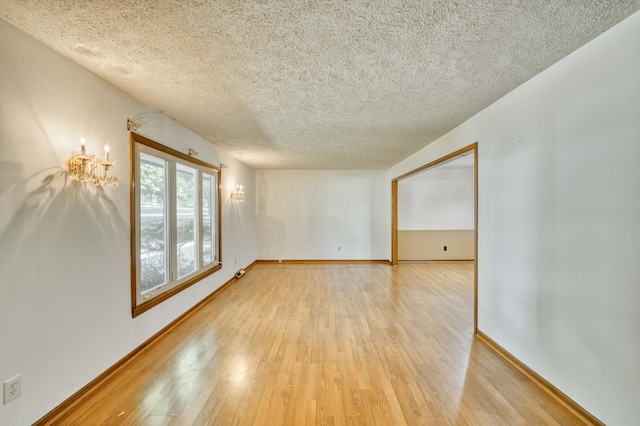 4852 S Charleston Ave, Springfield, MO 65804 - spare room featuring light wood-style floors, a textured ceiling, a chandelier, and baseboards