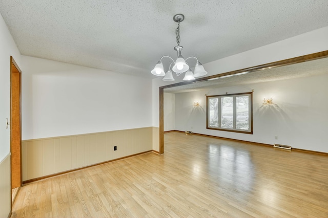 4852 S Charleston Ave, Springfield, MO 65804 - empty room featuring wood finished floors, a textured ceiling, a chandelier, and wainscoting