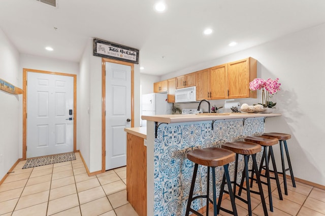 kitchen featuring white appliances, a breakfast bar, light tile patterned flooring, and recessed lighting