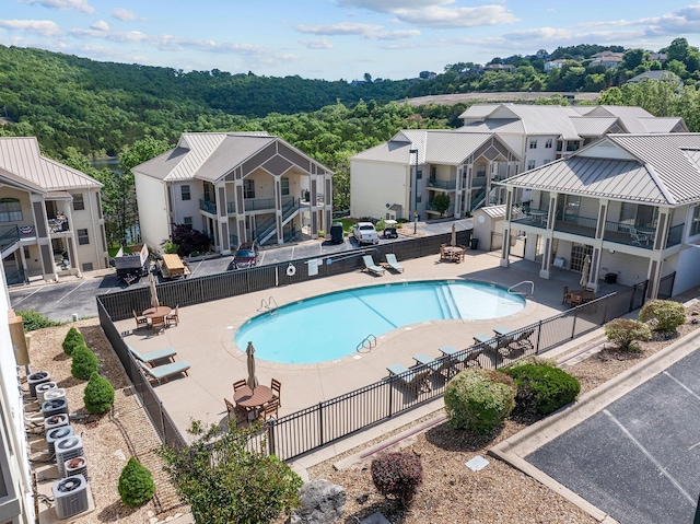 community pool with fence, central air condition unit, a patio area, and a residential view