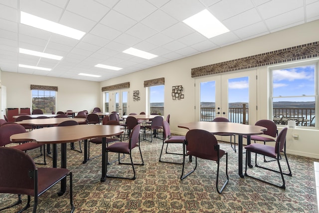carpeted dining room with french doors, a paneled ceiling, and baseboards