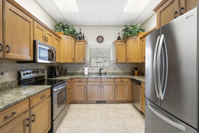 kitchen featuring appliances with stainless steel finishes, a sink, a drop ceiling, brown cabinetry, and backsplash