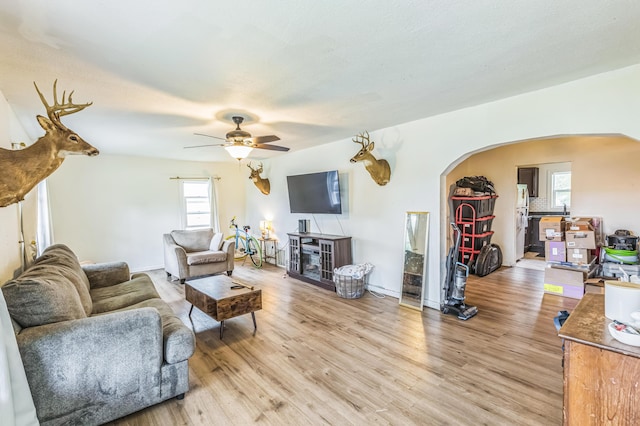 living room featuring arched walkways, light wood-type flooring, ceiling fan, and baseboards