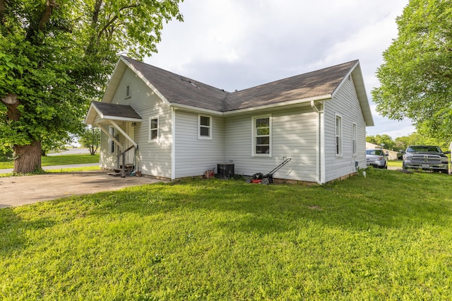 back of house with entry steps, a lawn, central air condition unit, and a shingled roof