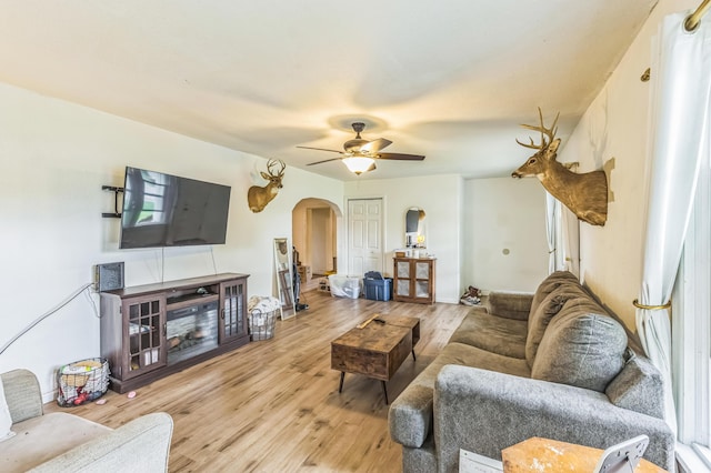 living area featuring arched walkways, light wood-style flooring, and ceiling fan