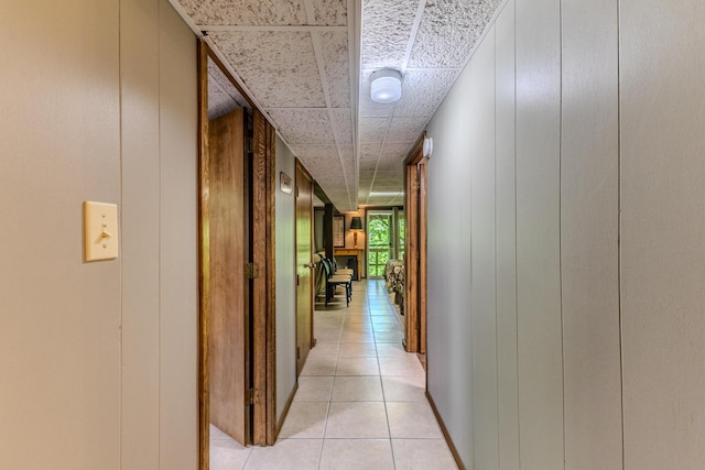 hall featuring light tile patterned floors, a decorative wall, and a paneled ceiling