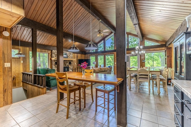 dining room featuring wooden walls, light tile patterned floors, a chandelier, wood ceiling, and a stone fireplace