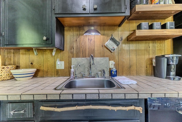 kitchen featuring tile counters, a sink, wood walls, and black dishwasher