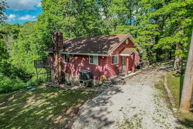 view of front facade featuring a chimney, central AC, gravel driveway, a shingled roof, and a wooded view