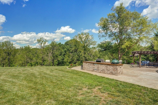 view of green lawn featuring exterior kitchen, a pergola, a patio area, and a wooded view