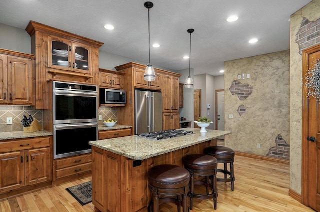 kitchen featuring appliances with stainless steel finishes, light wood-style floors, brown cabinets, a breakfast bar area, and recessed lighting
