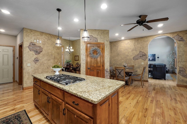 kitchen featuring stainless steel gas cooktop, arched walkways, light wood-style floors, ceiling fan, and light stone counters