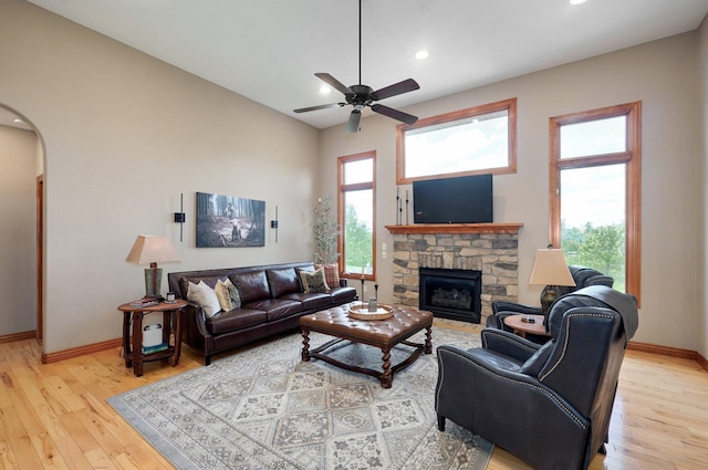 living area with arched walkways, light wood-style flooring, a stone fireplace, a ceiling fan, and recessed lighting